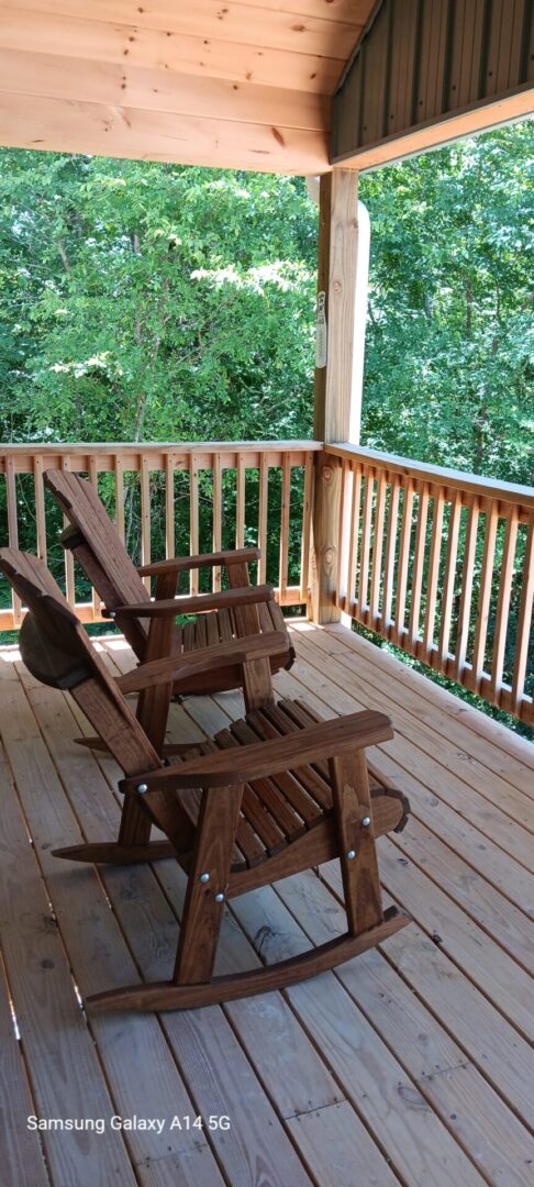 Two wooden chairs on a deck with trees in the background.