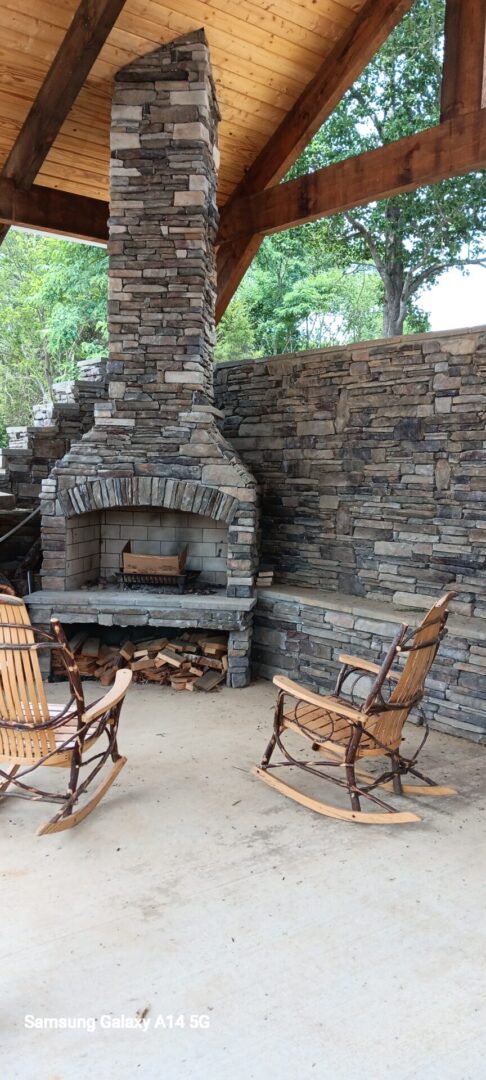 A stone fireplace with two chairs and wood logs.